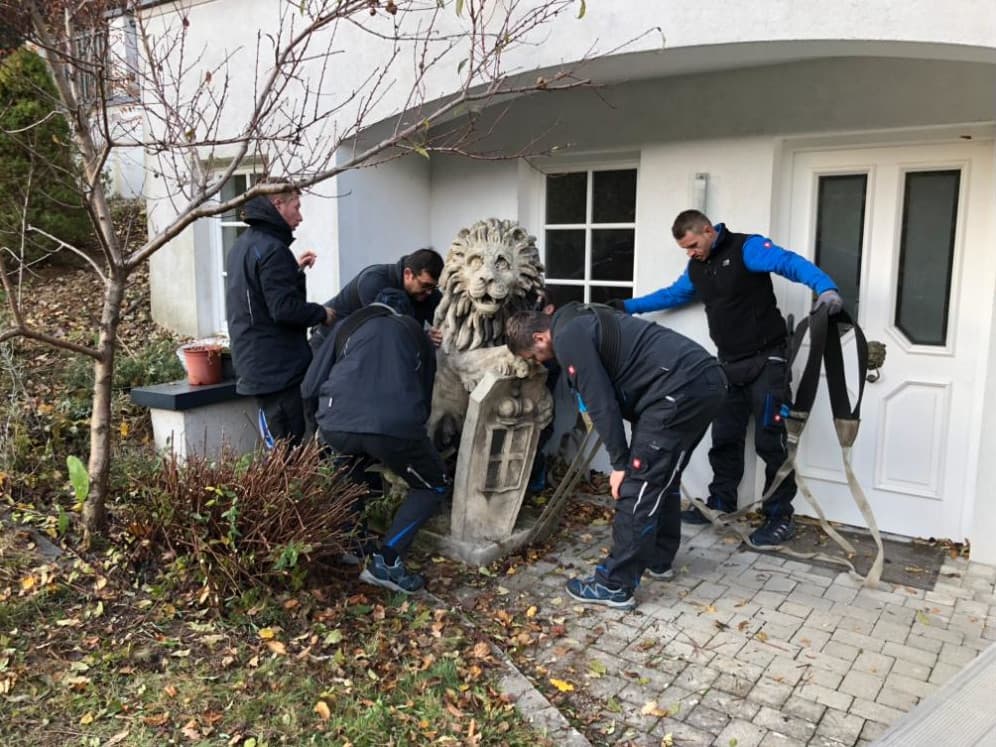 A-Team-Mitarbeiter bewegen gemeinsam eine schwere Löwenskulptur